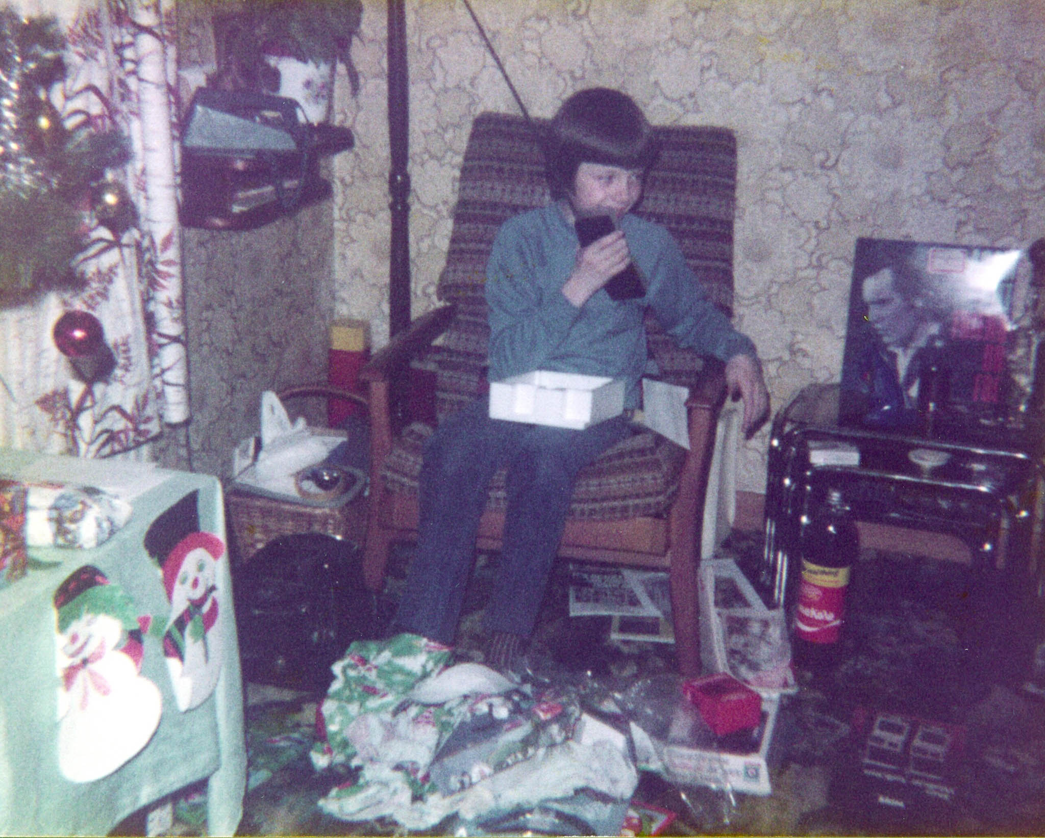 Young boy aged around 10 on a chair in the living room on Christmas morning. He's talking into a walkie talkie that was clearly a Christmas present. There are presents at his feet and an Adam Ant record beside him, Friend or Foe. 